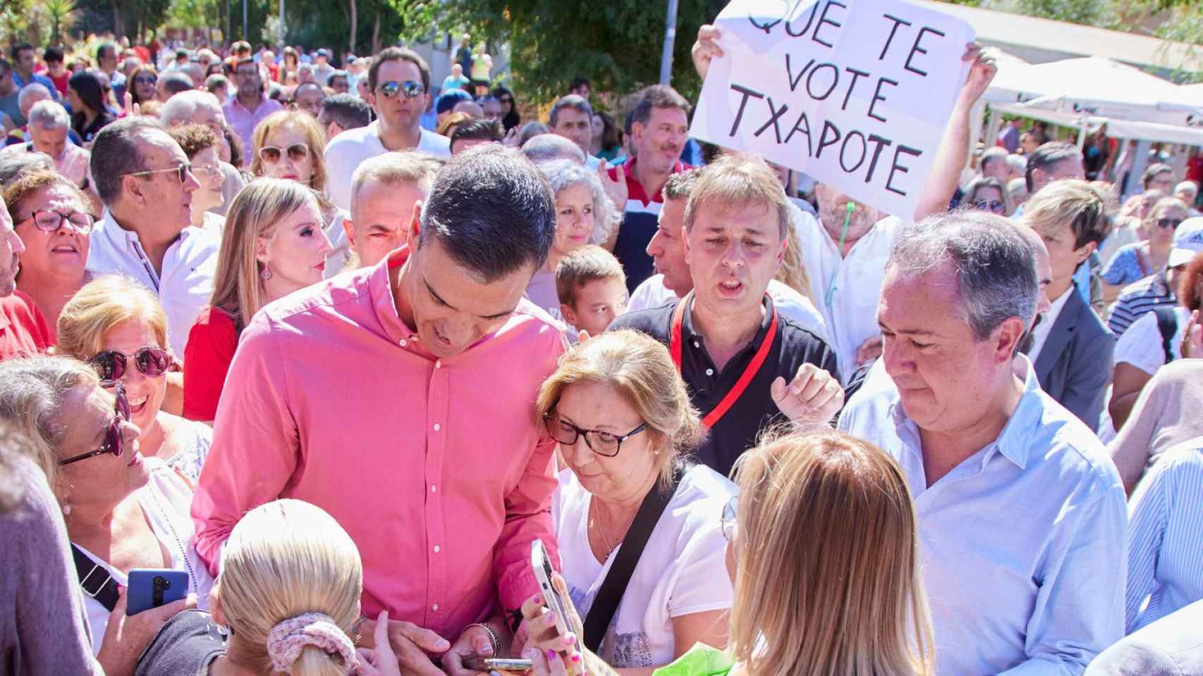 El presidente del Gobierno, Pedro Sánchez, junto a Juan Espadas, con la pancarta detrás: Que te vote Txapote.