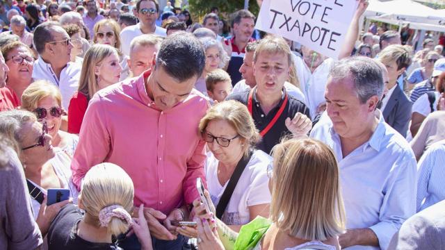 Pedro Sánchez junto a Juan Espadas en el sevillano barrio de Pino Montano, el 3 de septiembre de 2022. Al fondo, el creador anónimo del 'Que te vote Txapote' sujeta el cartel con el lema.