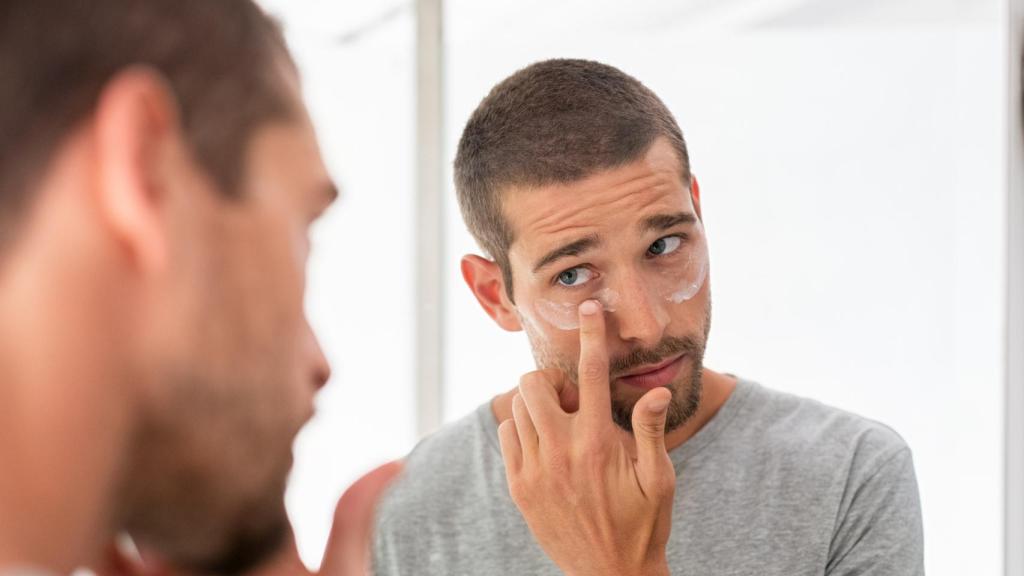 Un hombre poniéndose crema frente al espejo.