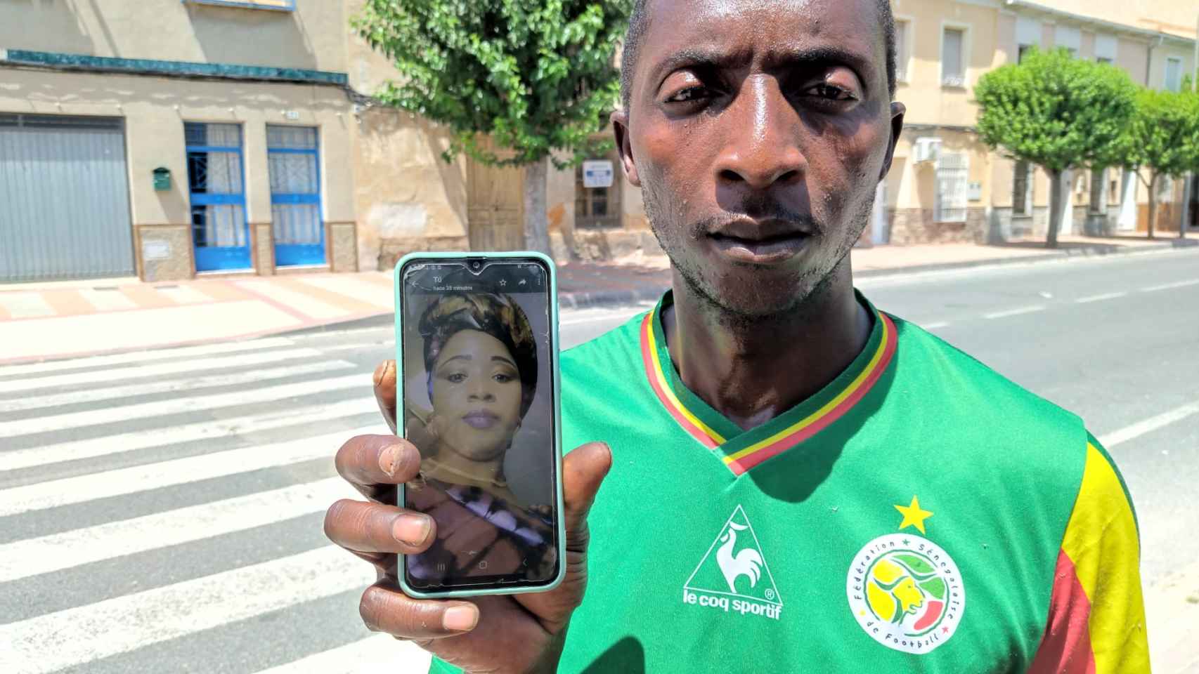 Khadj Sy, este lunes, mostrando una foto de su esposa, Astou, junto al paso de peatones donde fue atropellada.
