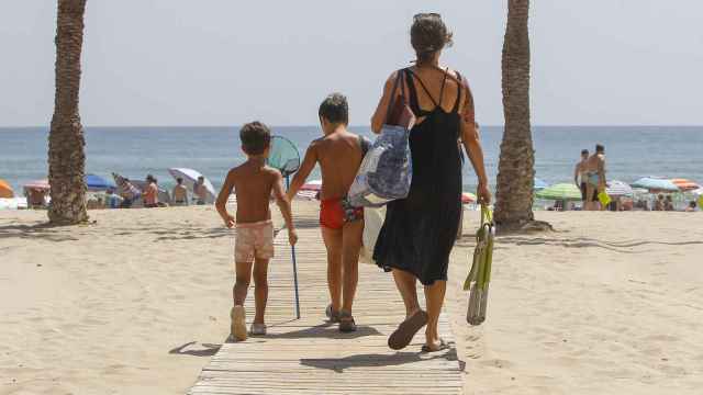 Tres personas se dirigen a la orilla de la playa de San Juan cuando la temperatura del Mediterráneo ya se sitúa en torno a los 28 grados.