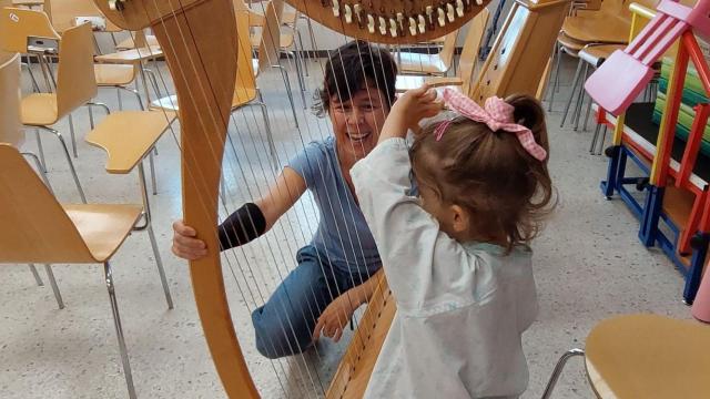 Una música enseñando a un niño hospitalizado el arpa en el Clínico de Santiago
