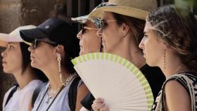 Varias personas se protegen del calor con gorras y abanico ante las elevadas temperaturas del verano.