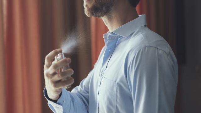 Un hombre se rocía con un perfume.