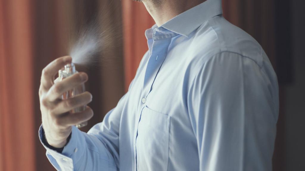 Un hombre se rocía con un perfume.