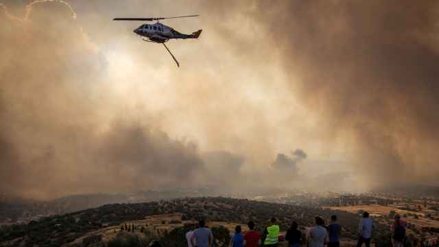 Un grupo de personas observan al helicóptero de los bomberos intentando sofocar las llamas en Mandra, Grecia.