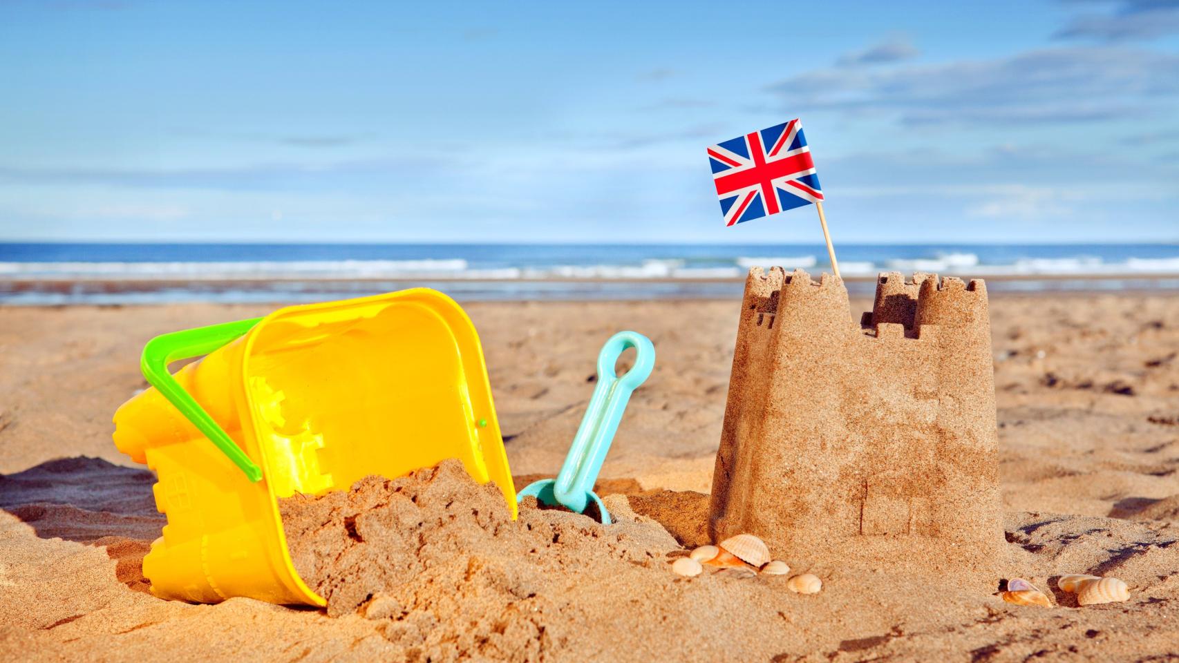 Un castillo de arena en la playa con una bandera de Reino Unido encima, en una imagen de archivo.