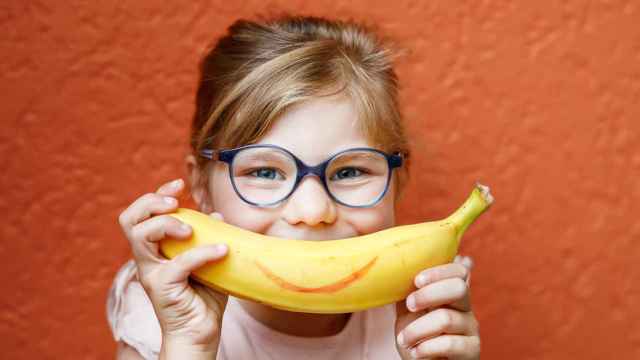 Imagen de archivo de una niña con un plátano como si fuera una sonrisa.