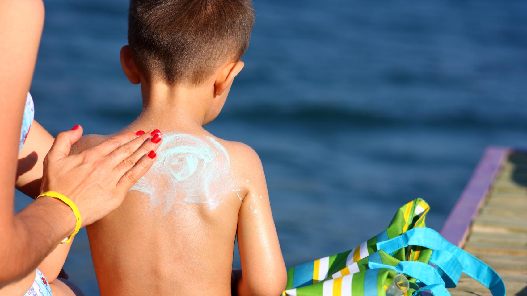 Una mujer aplica a un niño la crema solar en la playa.
