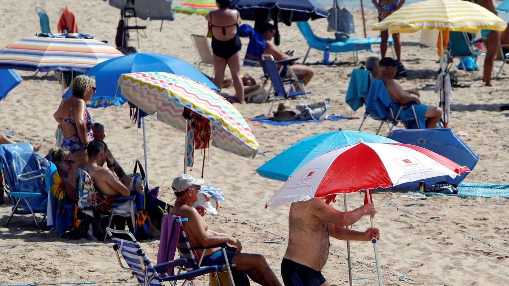 Varias personas con sombrillas en la playa.