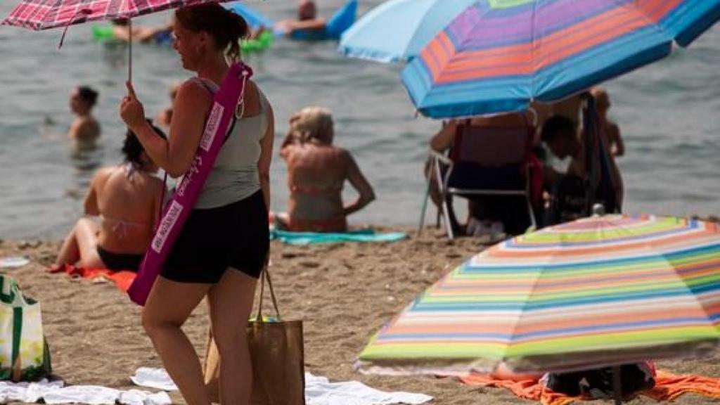 Una mujer con una sombrilla por la playa.