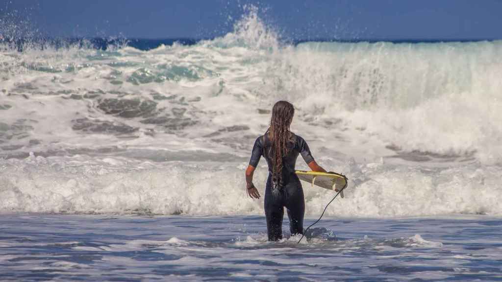 Una surfista se dispone a meterse en el mar para practicar este deporte.