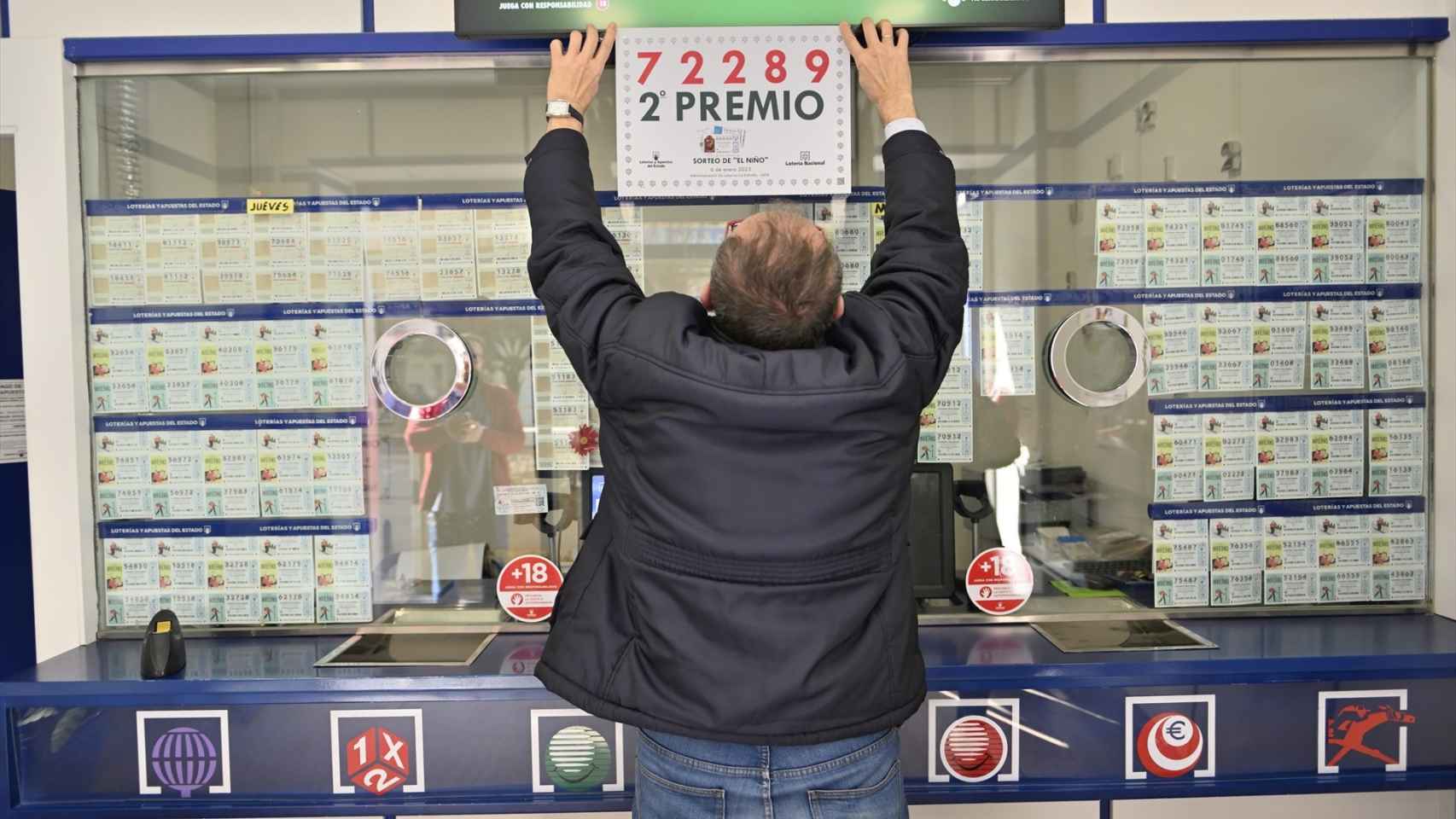Foto de archivo de un lotero de Jaén colocando el un cartel con el segundo número premiado de la Lotería del Niño 2023.