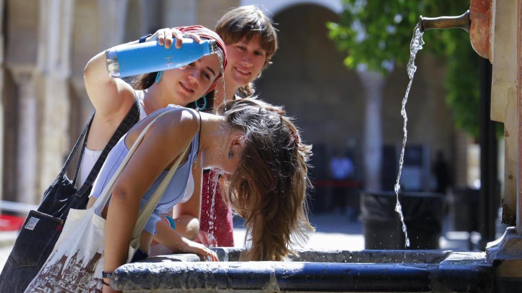 Unos niños se refrescan en una fuente de agua.