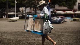 Una mujer llevando silla y sombrilla se dirige a la playa del Palo en Málaga.