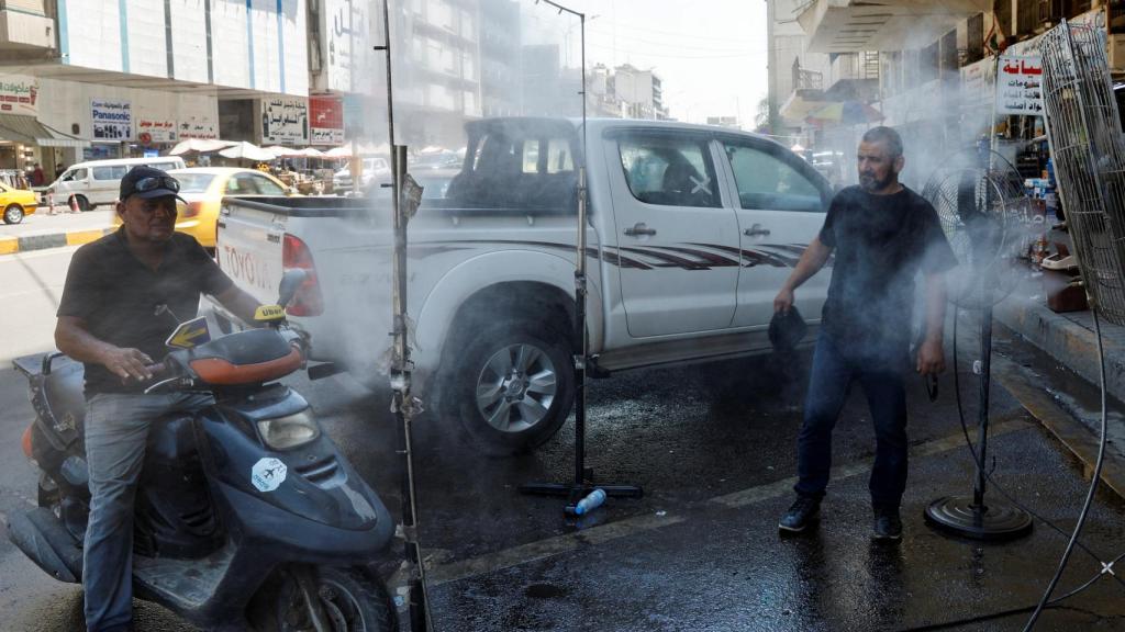 Hombres iraquíes parados frente a un ventilador en una calle para refrescarse en medio de una ola de calor en curso, en Bagdad.