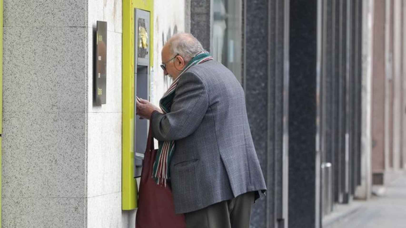 Un anciano sacando dinero de un cajero automático.