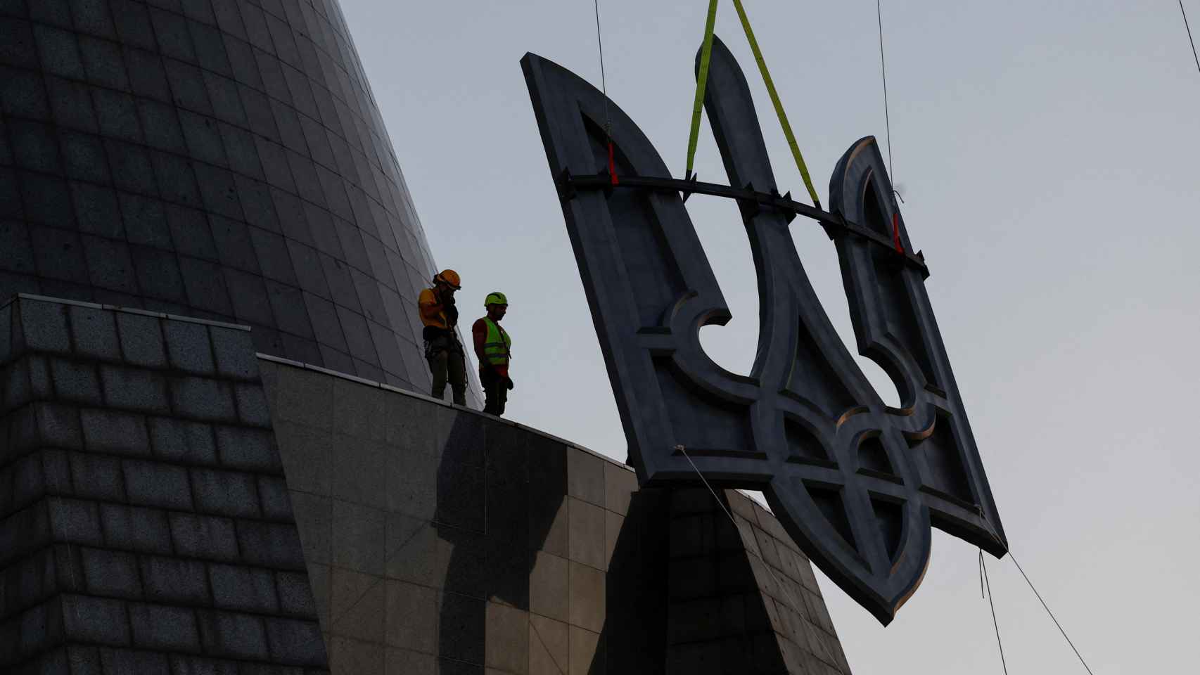 Unos trabajadores levantan el 'tryzub' ucraniano sobre el pedestal de la estatua de la Madre Patria.