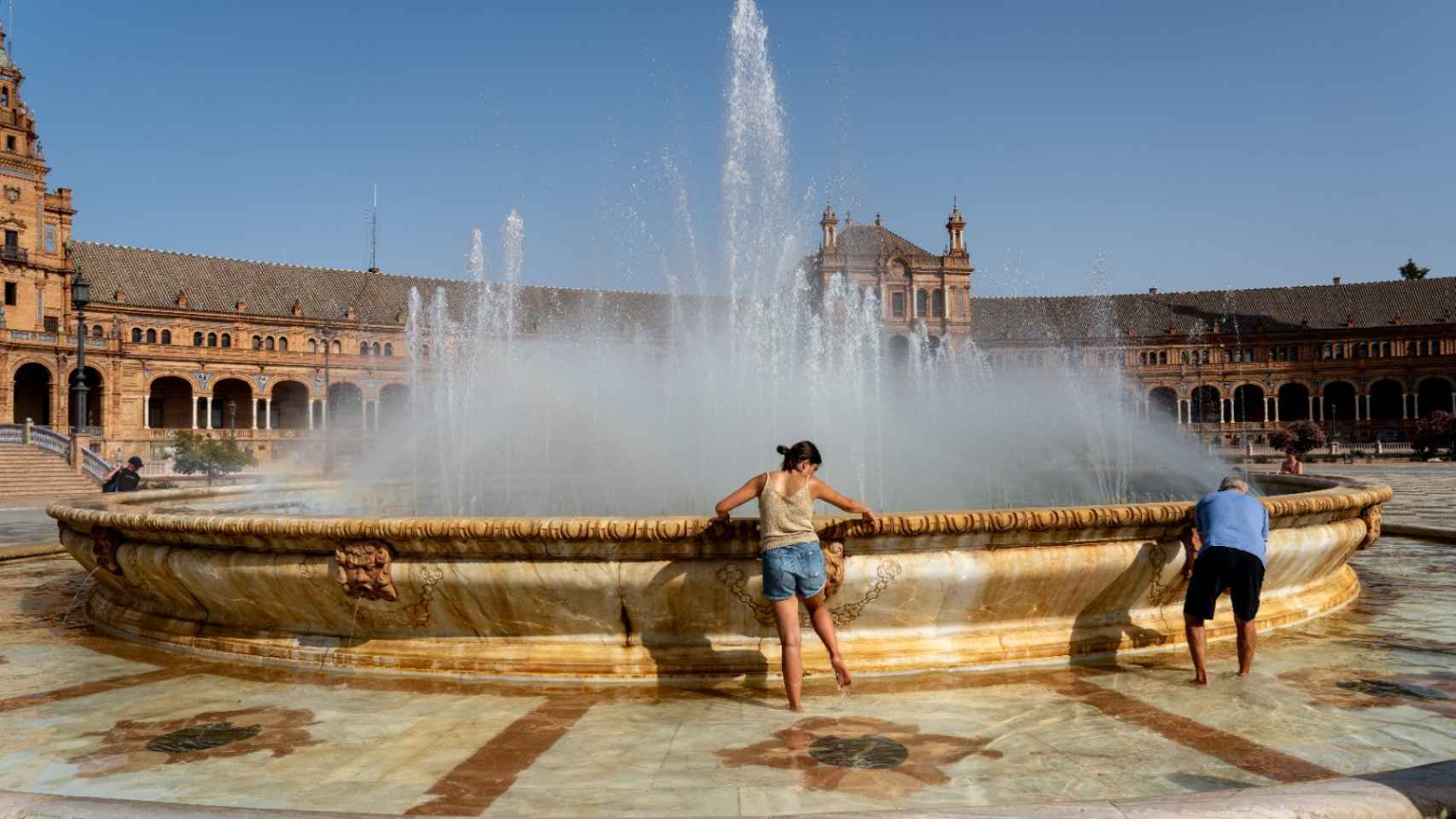 Dos personas intentan refrescarse en la fuente de la Plaza de España en Sevilla.