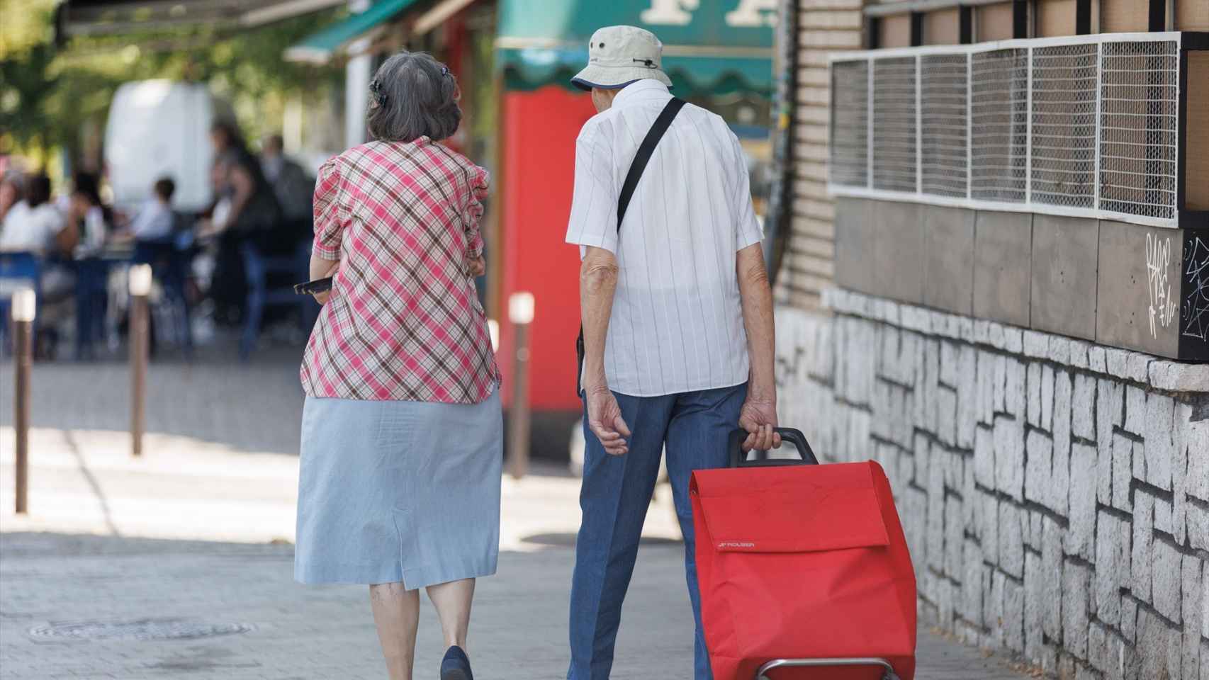Una pareja mayor camina con un carro de la compra.