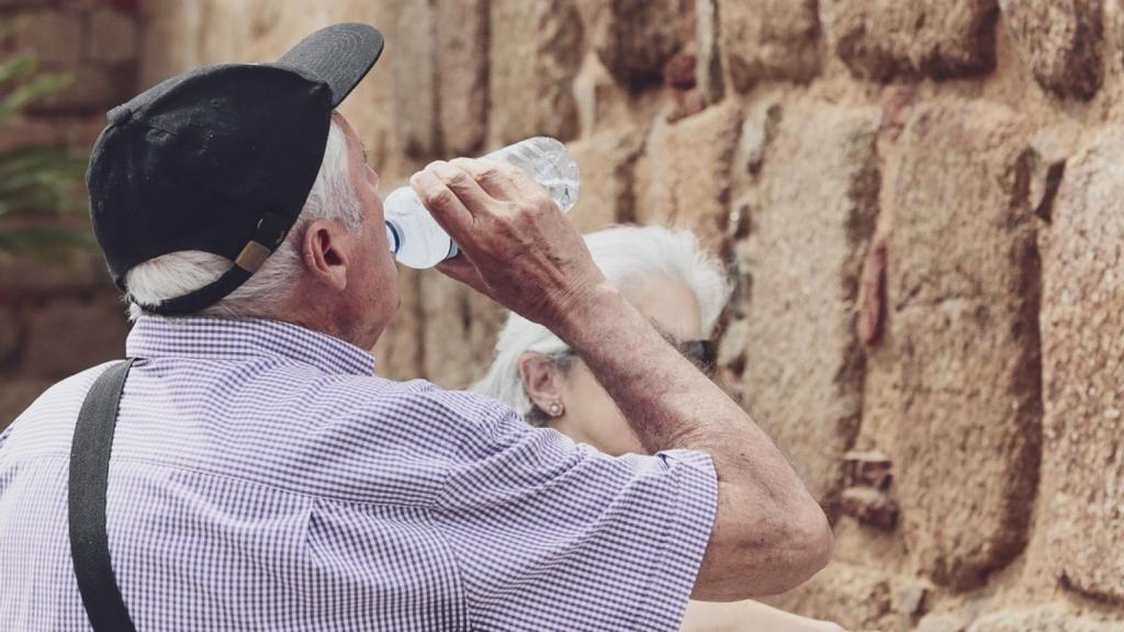 Un hombre mayor bebe agua de una botella en un día de intenso calor.