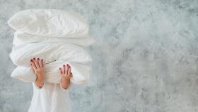 Imagen de archivo de una mujer sosteniendo ropa de cama y almohadas apiladas. Foto: iStock.