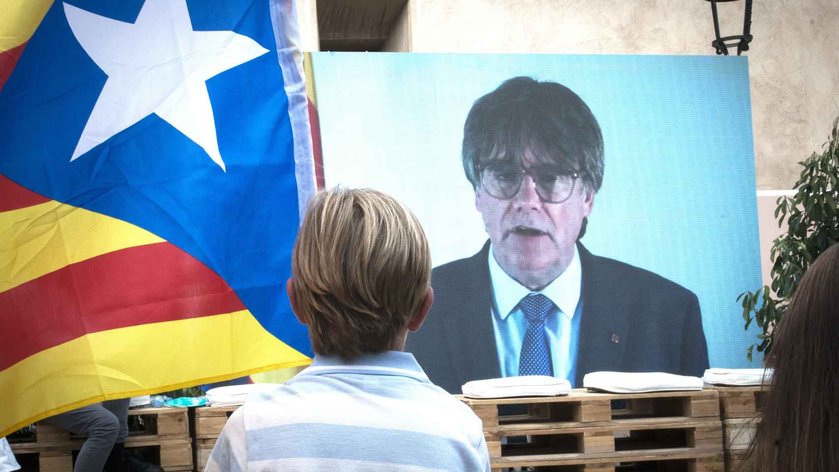 Un niño observa la intervención telemática de Puigdemont en un mitin de Junts en Gerona.