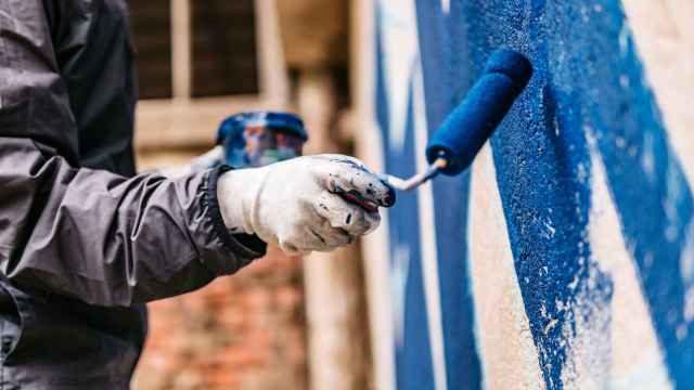 Un operario pintando de azul la pared de un edificio