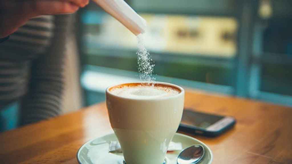 Una persona vierte azúcar sobre el café.