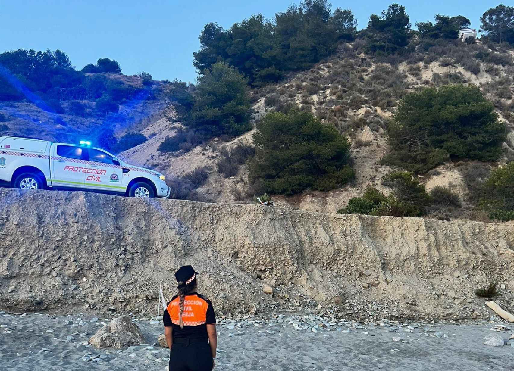 Una agente de Protección Civil en la playa acordonada mira hacia la furgoneta.