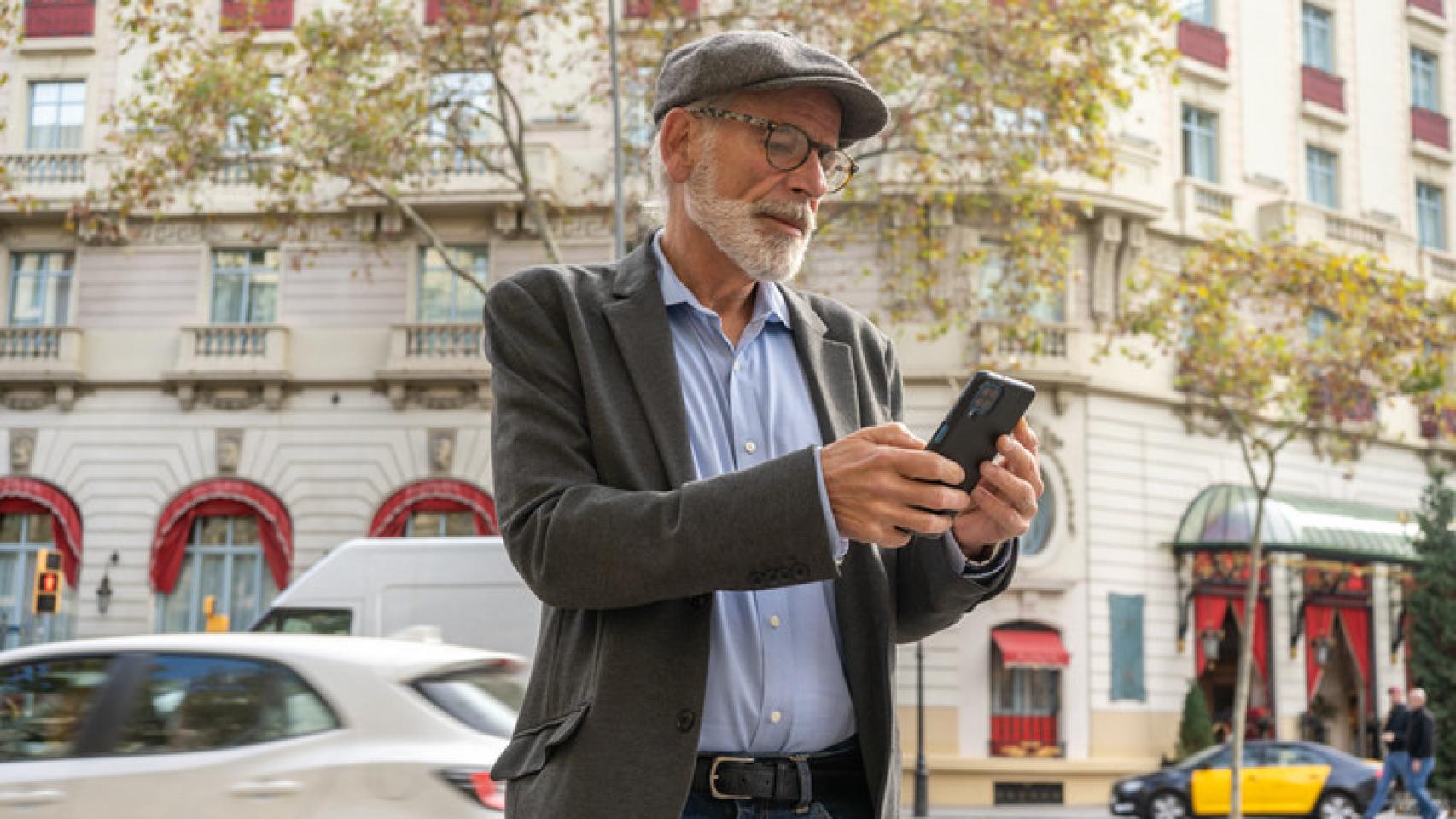 Un hombre mayor mirando el móvil en la calle.