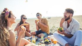 Un grupo de amigos disfruta comiendo en la playa.