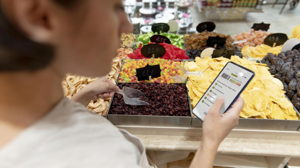 Una mujer busca en su teléfono el valor nutricional de unos alimentos del supermercado.