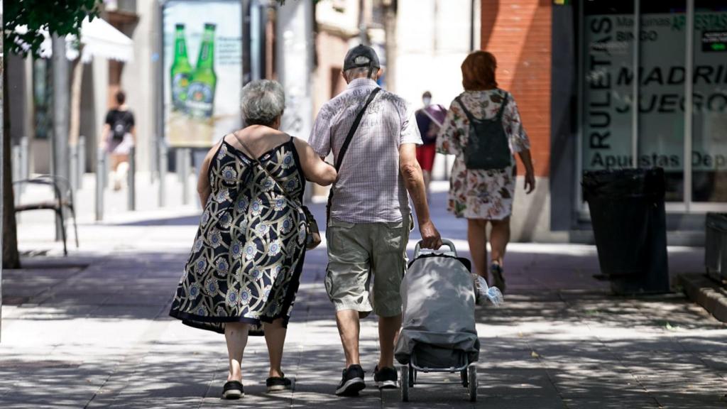 Una pareja de ancianos paseando con un carro de la compra.