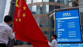 Bajada de la bandera de China delante de unas pantallas de valores bursátiles en Exchange Square.