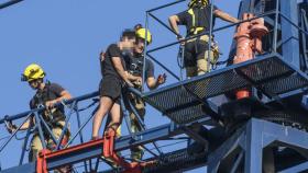 Tres bomberos ayudan al joven justo antes de empezar a bajar de la grúa