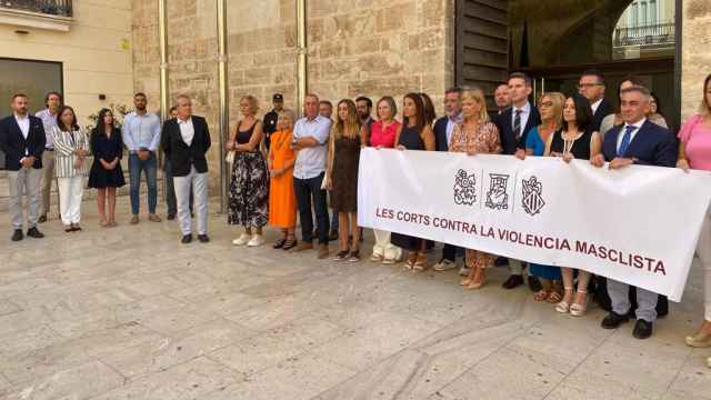 La presidenta de las Cortes Valencianas, Llanos Massó, a la izquierda junto a su grupo, ajenos a la pancarta. EE