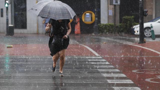 Una mujer camina por un paso de peatones bajo una intensa lluvia en Valencia.