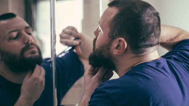 Imagen de archivo de un hombre recortándose la barba frente a un espejo.