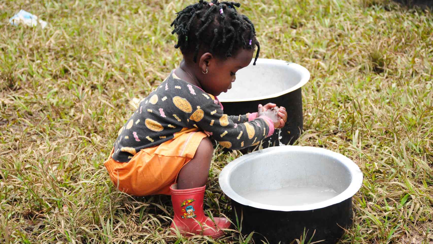 Una niña se lava cuidadosamente las manos en unos barreños.
