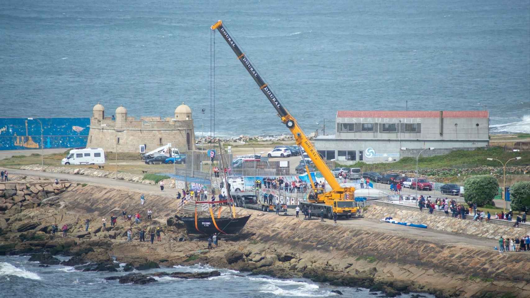 Una gran grúa retira la embarcación encallada en las rocas.