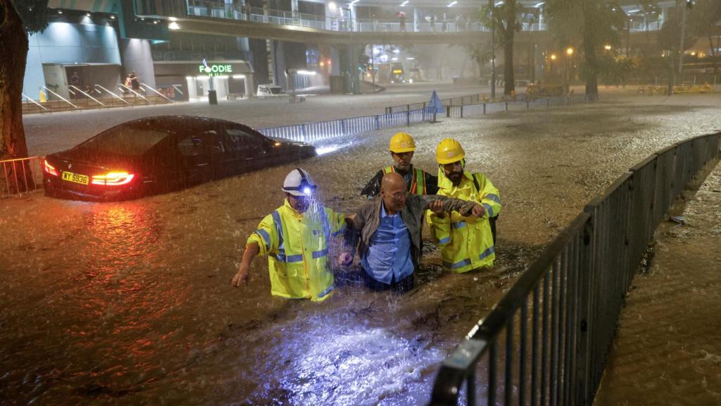 Servicios de emergencia ayudando a un hombre salir de una calle inundada.