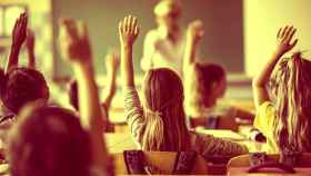 Unos alumnos de primaria levantan los brazos durante una clase.