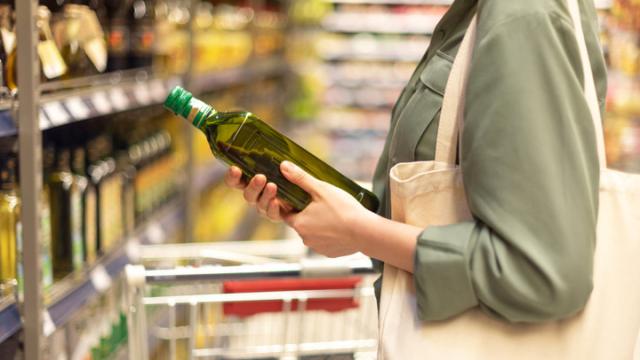 Una mujer elige una botella de aceite en el supermercado.