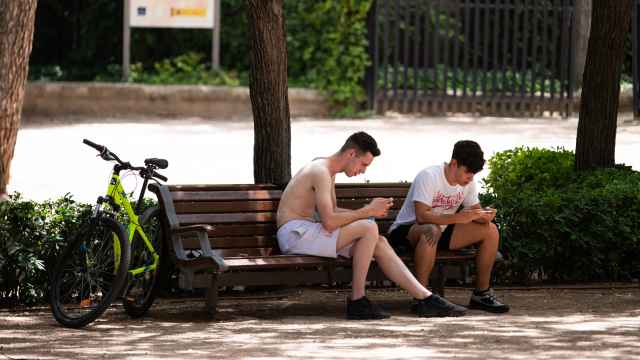 Dos jóvenes utilizando el móvil en un parque.