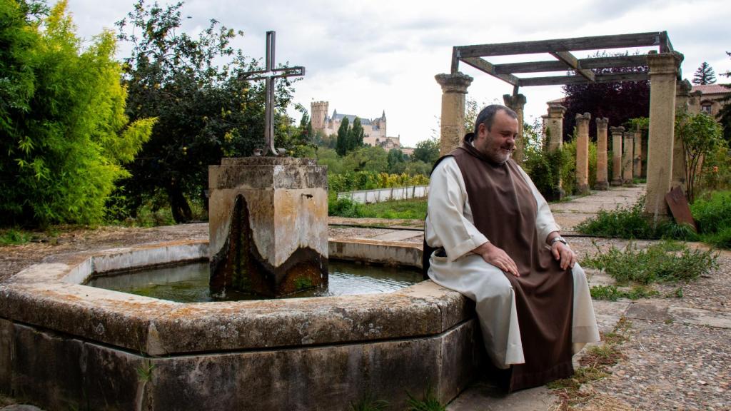 El prior, fray Mauro, sentado en la fuente del jardín del monasterio; de fondo, el Alcázar de Segovia