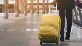 Una viajera con una maleta de ruedas amarilla en el aeropuerto.
