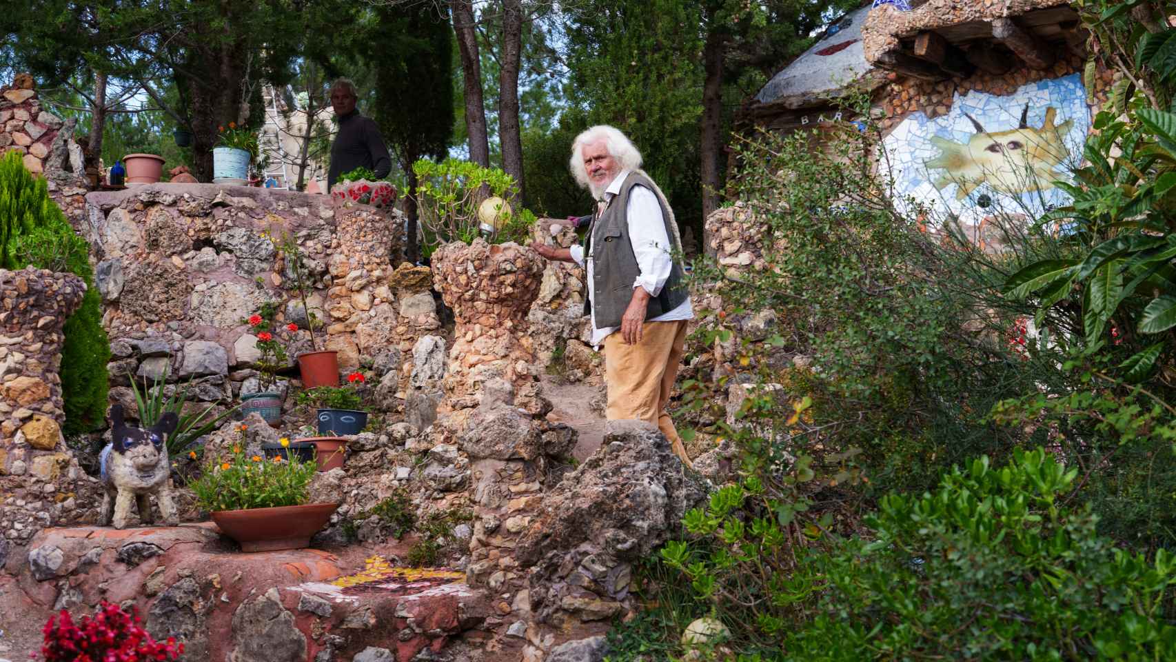 Peter Buch camina por su jardín de figuras; al fondo, ensombrecido, su hijo, Orson Buch