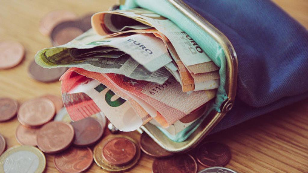 Imagen de un monedero lleno de billetes de euro y monedas alrededor.