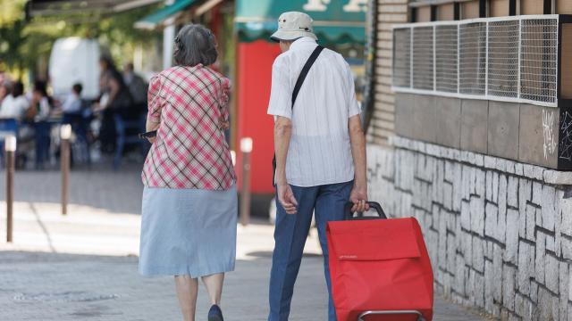 Una pareja mayor caminan con un carro de la compra.